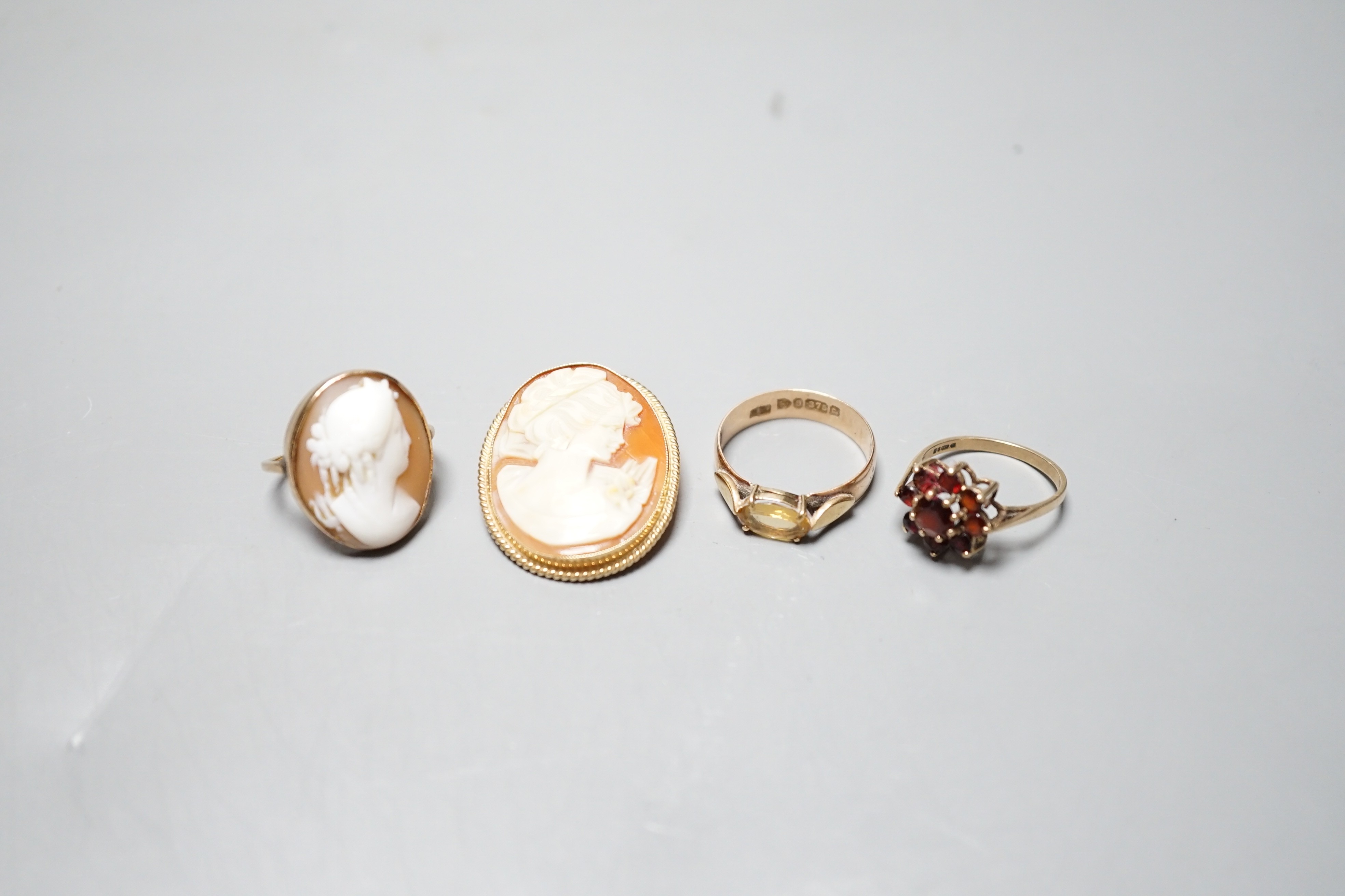 A late Victorian 9ct gold and citrine set ring, size S/T, a modern 9ct gold and garnet cluster set ring, a modern 9ct gold mounted oval cameo shell brooch and a yellow metal and cameo shell set dress ring, gross weight 1